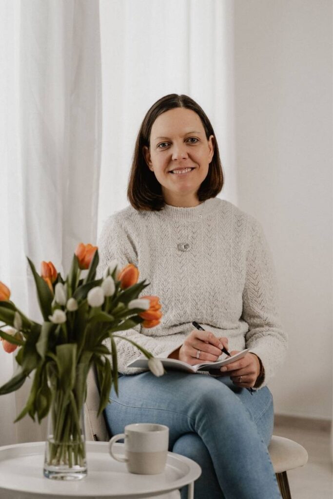 Frau sitzt mit Blumen und Tasse auf Tisch und macht Notizen